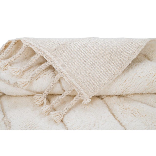 Artistic hand-knotted wool rug featuring an elongated diamond pattern in a soft Ivory tone. with its plush texture and...