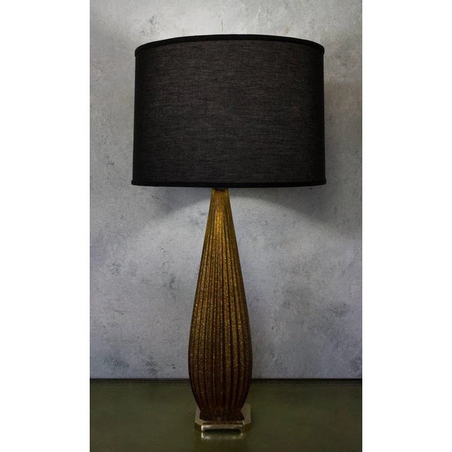 This Italian Murano table lamp features a ribbed glass body infused with shimmering gold flecks that create a warm,...