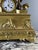 An important Empire period clock in gilt and patinated bronze, depicting a draped male figure in the antique style, seated...