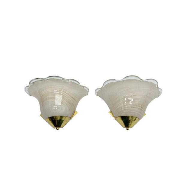 A set of shell-shaped glass wall sconces of Italian origin with a wavy edge and a brass mount. The glass features a white...