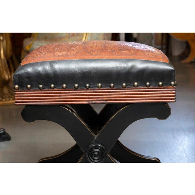 This is one of a pair of handsome ottomans featuring a richly tooled saddle-brown leather seat with an intricate foliate...