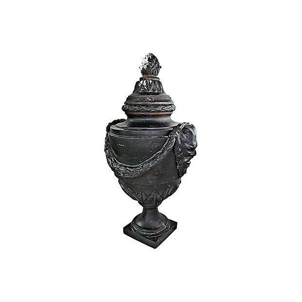 Cast iron lidded urn with a baroque motif and a removable cap topped by a pineapple knob. No maker's mark. Some finish wear.