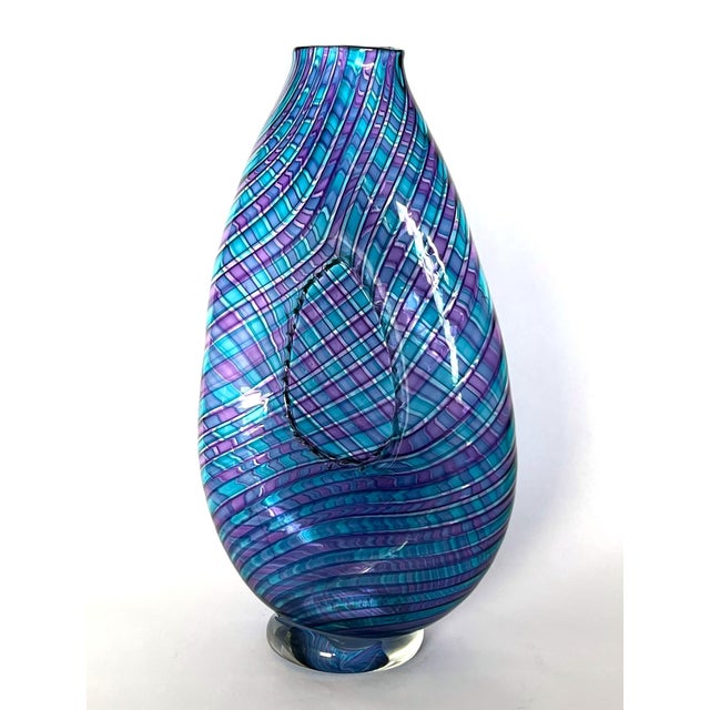 The handblown glass bottle in a tall, flattened, tapering shape with gently flared mouth and rounded lower body is...