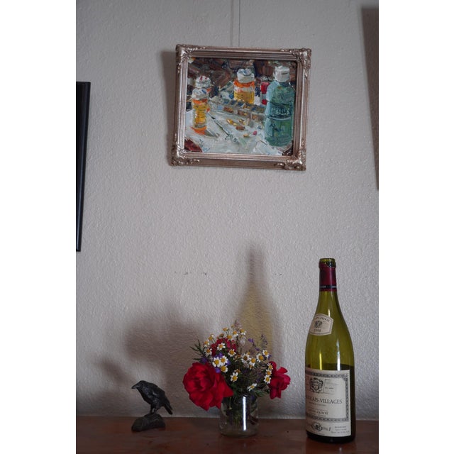 This oil on panel work depicts a cluttered table strewn with prescription bottles and medical paraphernalia, evoking a...