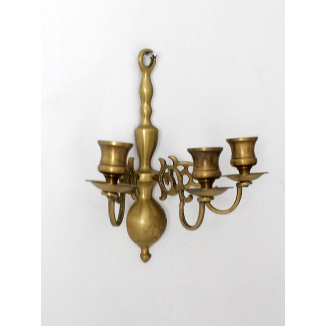 Vintage 1960s brass wall candle sconce featuring a three-arm candelabra design with ornate scrollwork, curled arms, and a...