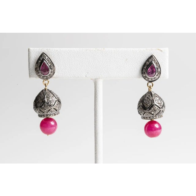 A pair of pave`-set, round-cut diamonds set in sterling silver with a faceted, pear-shaped ruby on the post also...