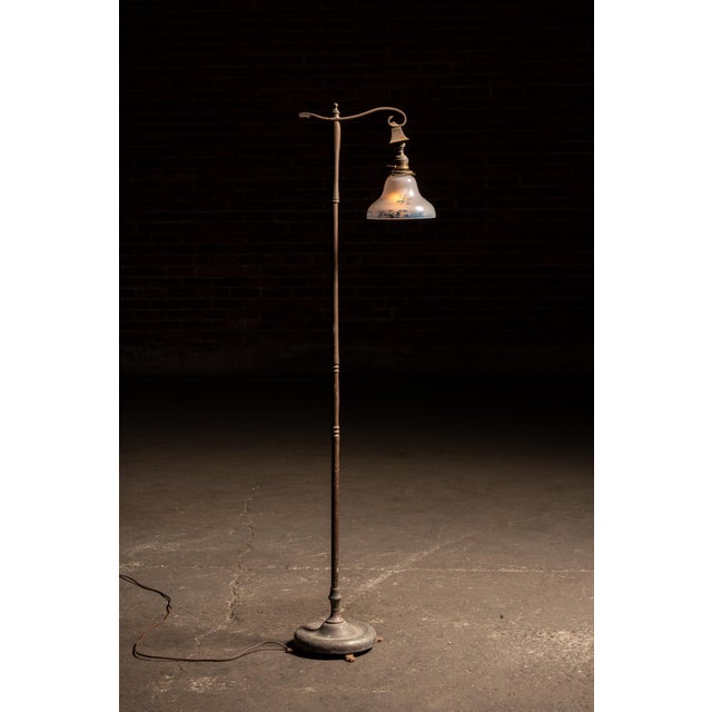 Floor lamp featuring a turned metal standard rising from a weighted round base with four small feet. The upper arm...