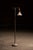 Floor lamp featuring a turned metal standard rising from a weighted round base with four small feet. The upper arm...
