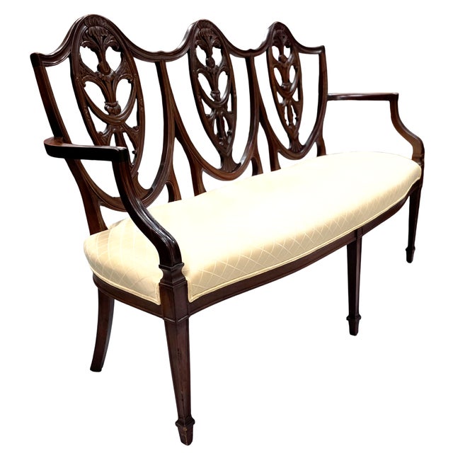 Featured is a Antique Mahogany Shield-Back Settee. This elegant and finely proportioned piece boasts a beautifully carved...