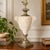 Sculptural vintage Neoclassical table lamp featuring an amphora-inspired ceramic body finished in mottled beige and cream...