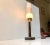 This is a torch shaped table lamp composed of rosewood with a brass top and an oblong pressed glass shade. It is designed...
