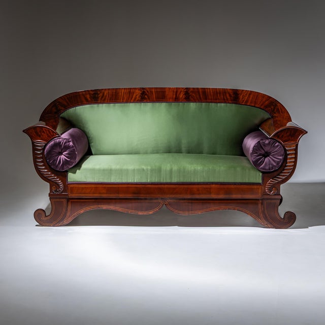 Biedermeier sofa with a shaped apron and rolled legs. The armrests are decorated with stylized cornucopias, while delicate...
