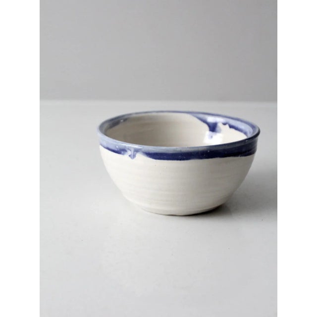 This is a vintage studio pottery bowl. Signed by the artist, the handmade white bowl has a blue drip glaze lip.