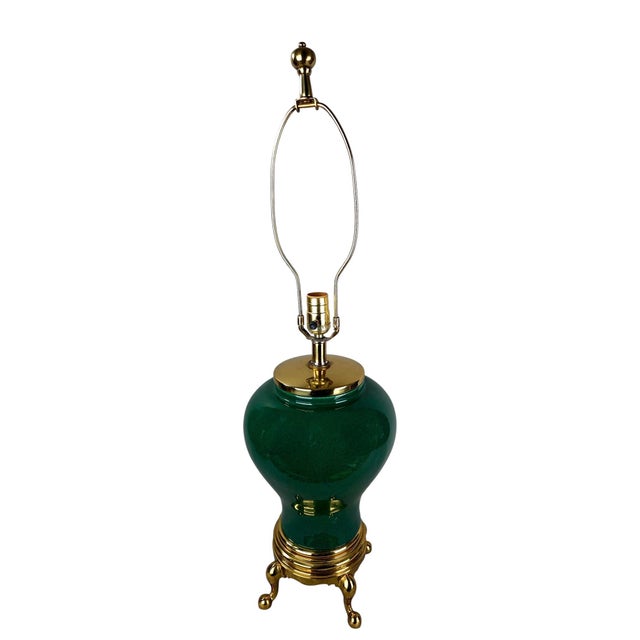 A ceramic table lamp in a deep emerald glaze, its bulbous ginger-jar body rising from a ribbed brass collar seated on...