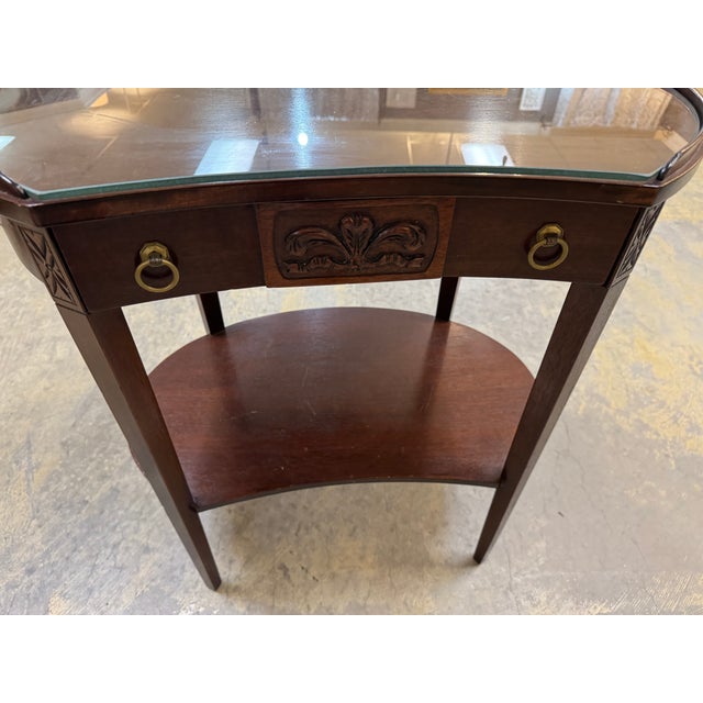 An antique mahogany Hepplewhite end table with a glass top and a drawer. The kidney-shaped tables in the image appear to...