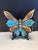 Hand-painted ceramic butterfly wall sculpture featuring rich turquoise, warm earth tones, and a glossy black ground....