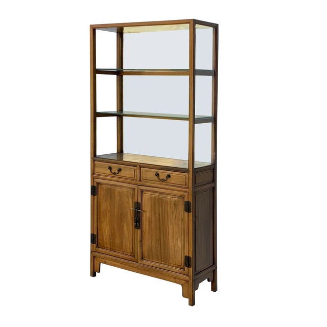 This is a simple light brown color display cabinet with two shelves and one bottom storage compartment. There is a mirror...