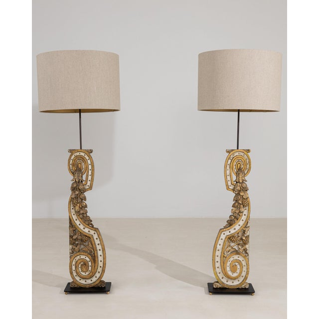 Pair of carved giltwood floor lamps in Antique Gold. The antique gold surface highlights ornate scrolled columns, linen...
