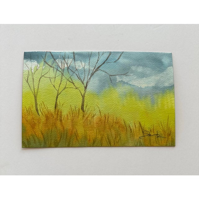 This serene watercolor painting captures the beauty of nature with soft hues of green, gold, and blue. Bare trees stand...