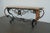 This vintage console table, likely dating to the late 20th century, pairs an intricately worked iron base with a richly...