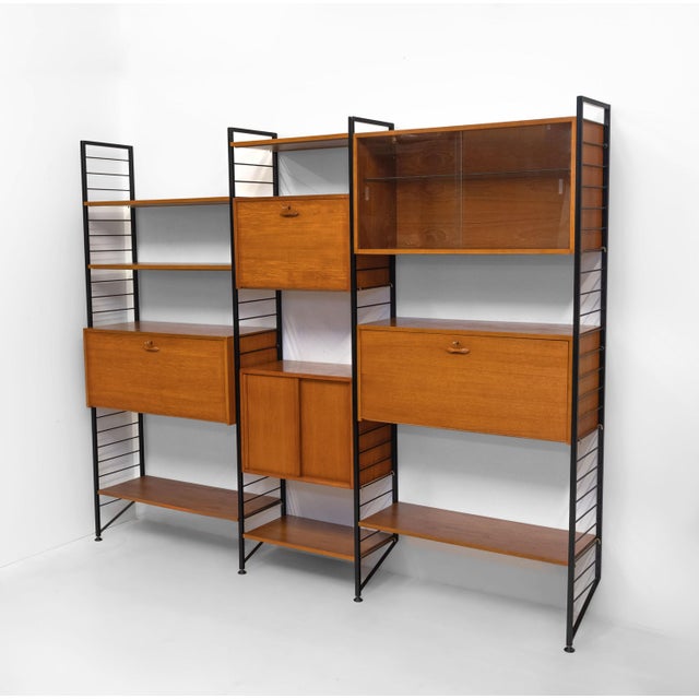 A substantial mid-century Ladderax teak and black metal six bay shelving system, with desk and cabinets. Designed by...