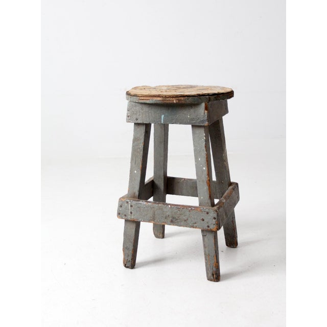 This is a vintage rustic wooden stool. The handcrafted wood stool features a well-worn paperboard seat and crackled gray...