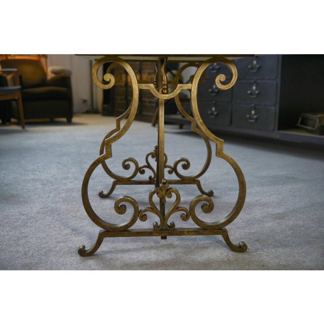 Wrought iron base with a dynamic design, partially gilded with gold leaf, topped with a warm-toned travertine tabletop....