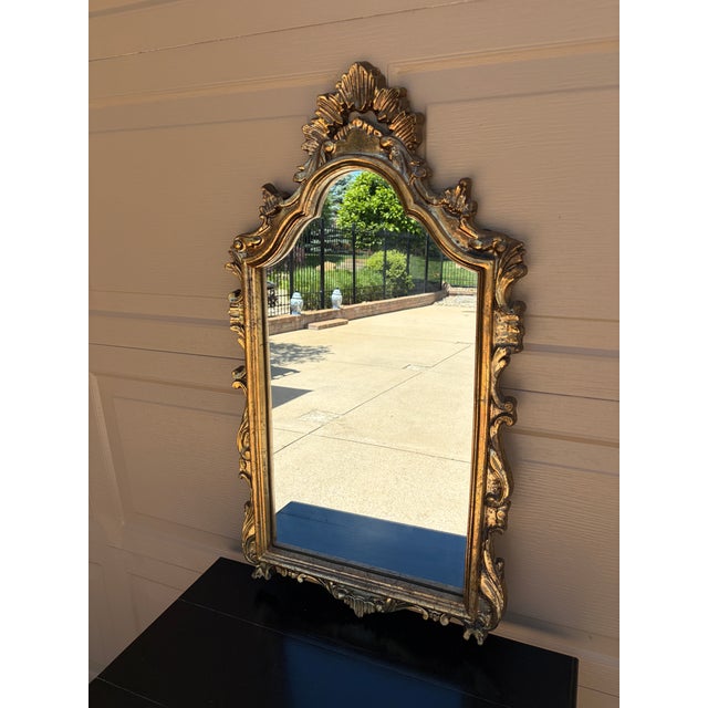 An elegant Italian giltwood mirror featuring a richly carved Rococo frame with scrolling acanthus details and original...