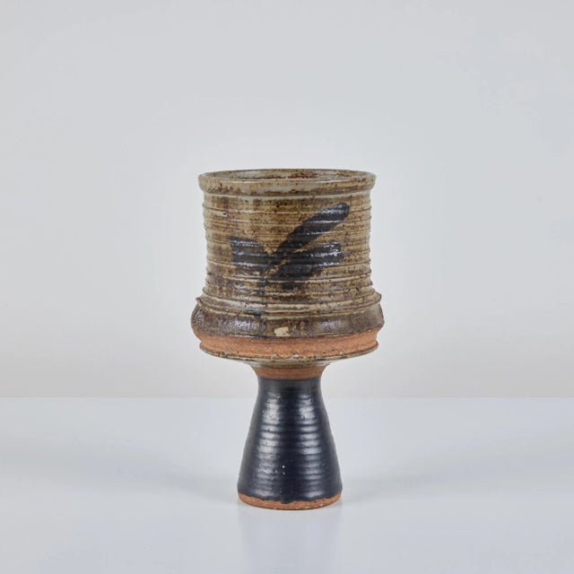 A tall, stoneware ribbed cylindrical vase with imperfect forest green glaze on the body's ribbed portion. This would...