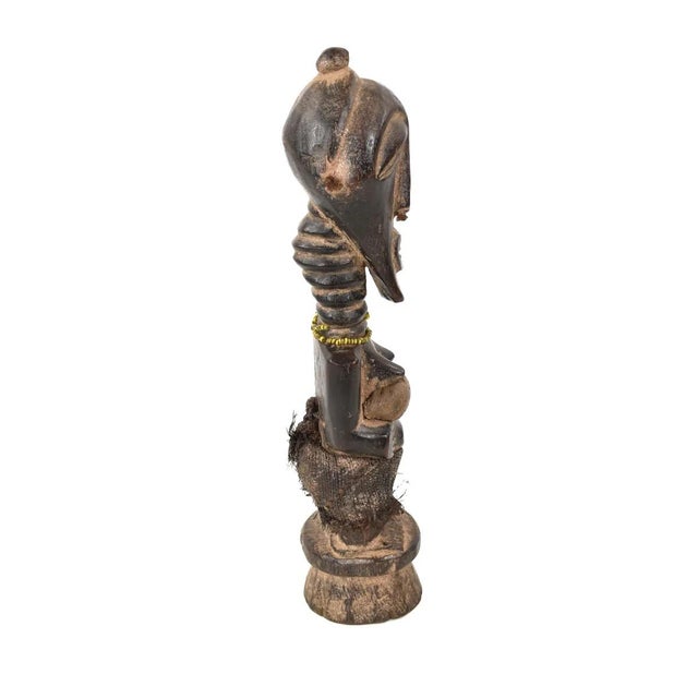 A standing Songye female power figure, known as Nkishi, exhibits a cylindrical neck, shoulders rounded, and arms elongated...