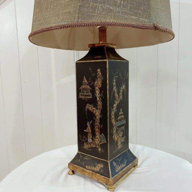 Vintage chinoiserie tole black lacquered lamp with a hand-decorated gilt design featuring pagodas, men, and flowers. A...