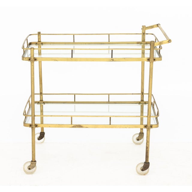 Mid-Century Modern Brass Two-Tier Bar Cart, with glass shelves on casters. 30.5" H x 31" W x 19.5" D. Provenance: From a...