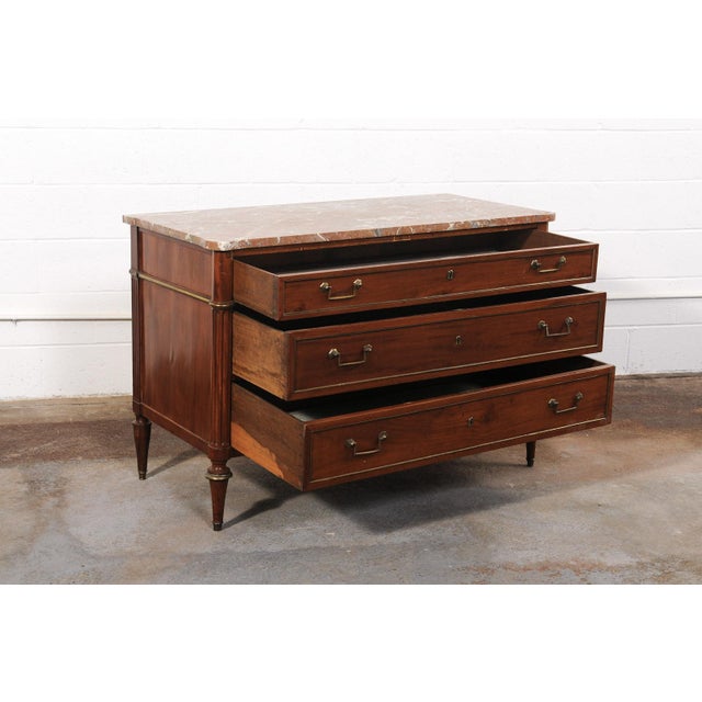 An elegant French Neoclassical period wooden commode with brass accents and marble top, dating from the early 19th...