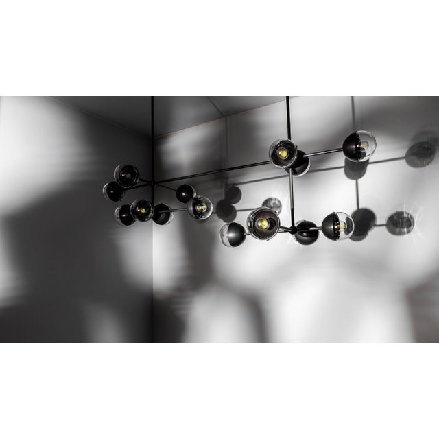 A fashionable line of enclosed bulbs expands into a playful configuration of elemental proportions. This chandelier of...