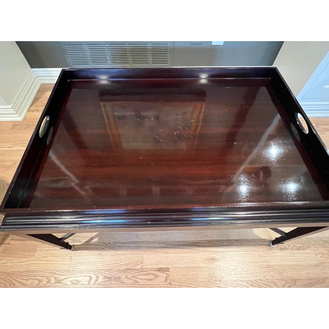 This dark mahogany-finished wood coffee table has a rectangular tray-style top with raised edges and integrated side...
