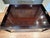 This dark mahogany-finished wood coffee table has a rectangular tray-style top with raised edges and integrated side...