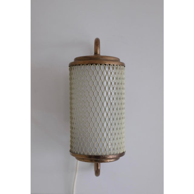 Charming Swedish Modern Wall lamp made out of expanded metal and brass. The metal creates a mesh design in off white with...