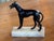 19th century dark patinated metal greyhound standing alert with mouth open and tongue showing, wearing a buckled collar,...