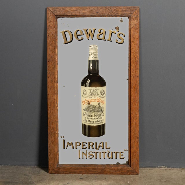Antique 20th Century rare advertising mirror. This 1930s oak framed advertising mirror shows a bottle of John Dewar & Sons...