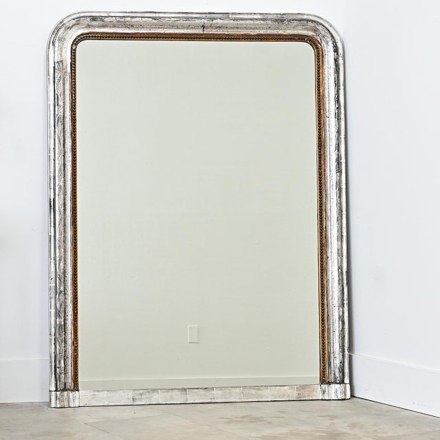 A French 19th century Louis Philippe mantel mirror in an arched, silver gilt frame enhanced by dark oxidation and...