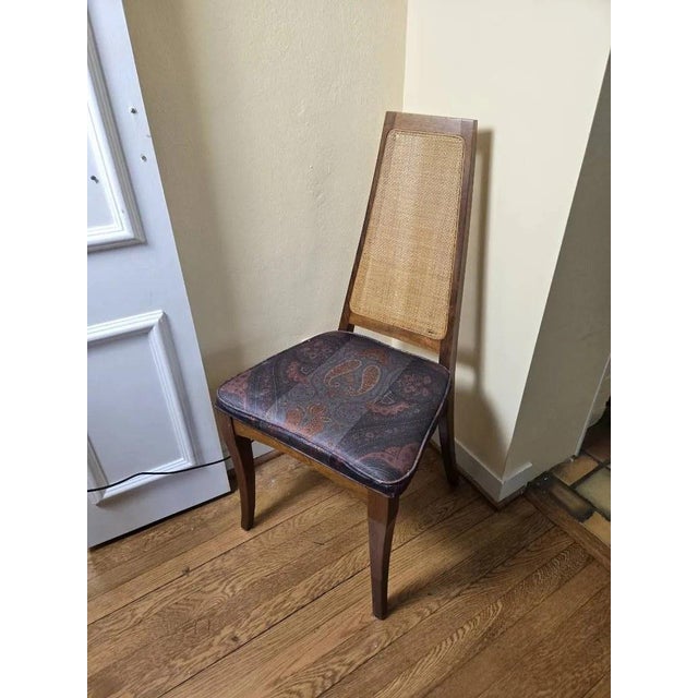 Four tall mid-century dining chairs with woven cane backs, tapered walnut-tone frames and upholstered seats. Details: -...