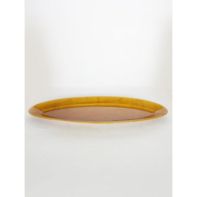 An elegant oval glazed ceramic serving platter featuring a warm gradient of browns and ochre—characteristic of French...