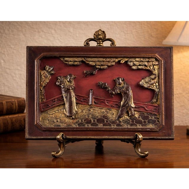 Chinese carved architectural wood panel featuring a figural courtyard scene with traditional dress, foliage, and stylized...