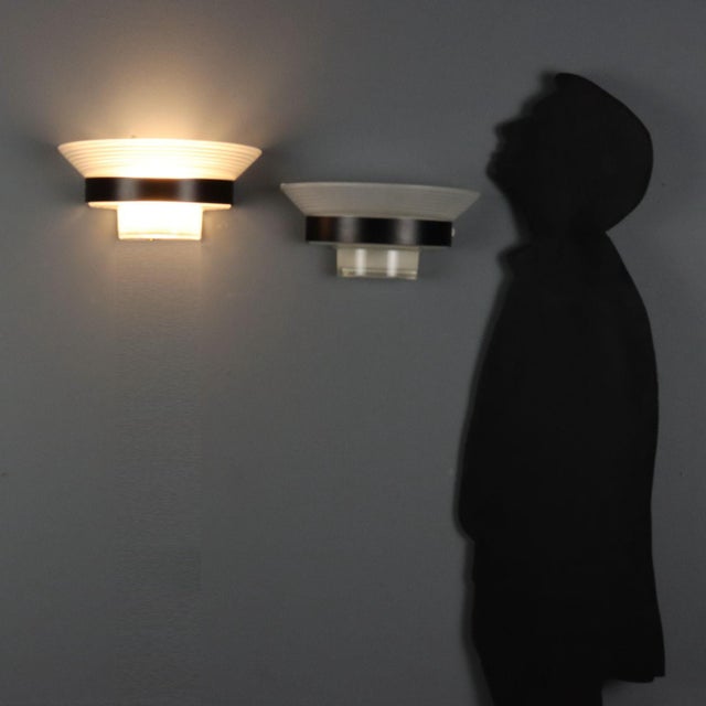 Wall lamps with enamelled metal structure and white and transparent glass diffuser. This piece is attributed to the...