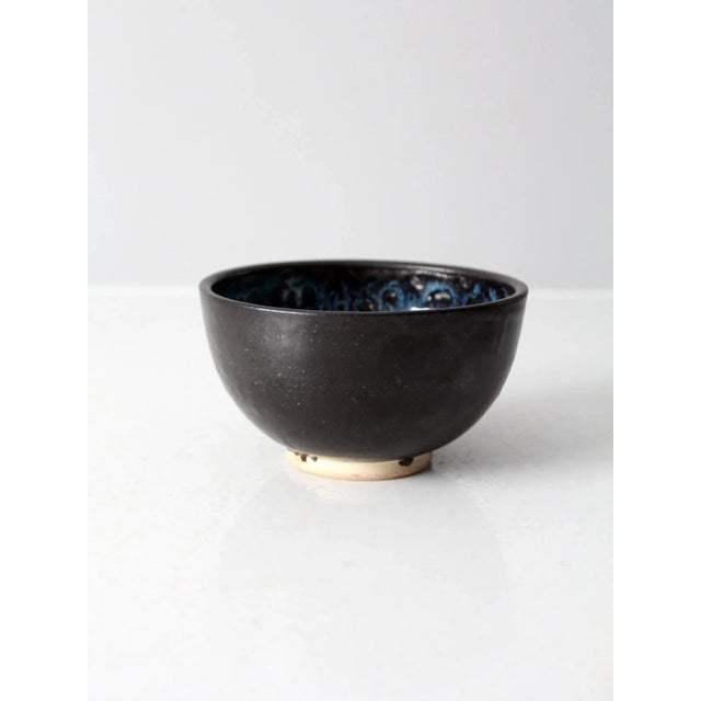 This is a vintage studio pottery bowl. Signed by the artist, the handmade ceramic bowl has a black exterior with striking...