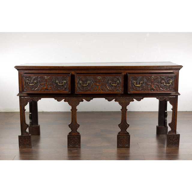 An English oak sideboard from the 19th century with three low-relief carved drawers, carved legs and brass hardware....