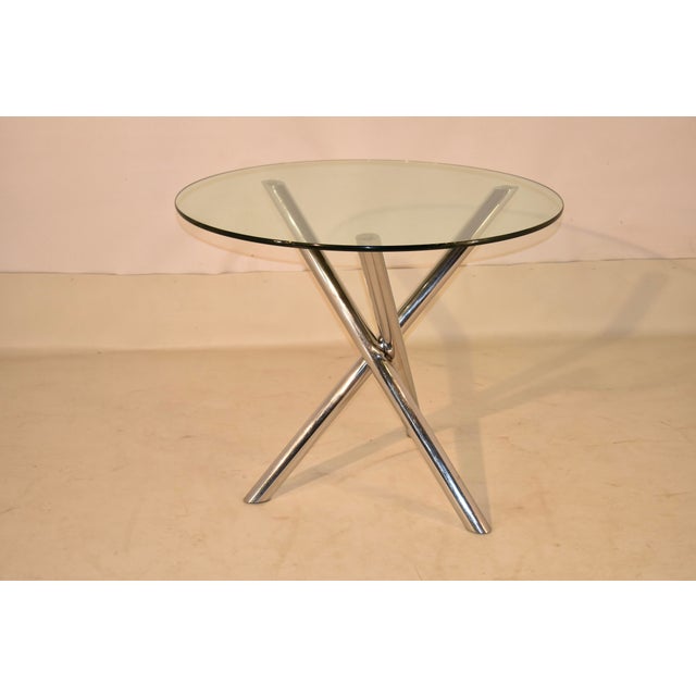 Mid-Century modern breakfast table with a glass top. The table has a three legged chrome base, with the legs intersecting...