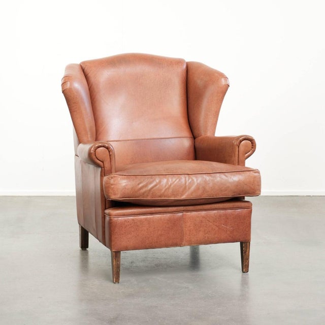 This light cognac-colored cowhide wing armchair has a characterful English look and is finished with matching piping and a...