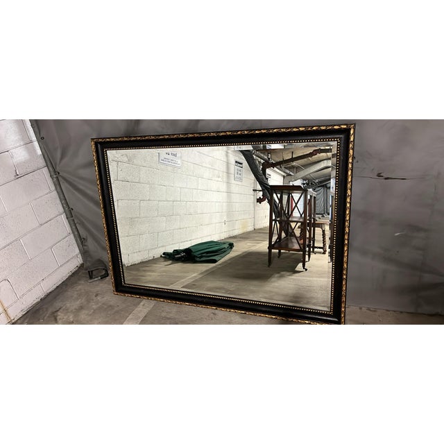 Stunning large wall mirror featuring a black frame with elegant gold gilt trim — a leaf/laurel motif along the outer edge...