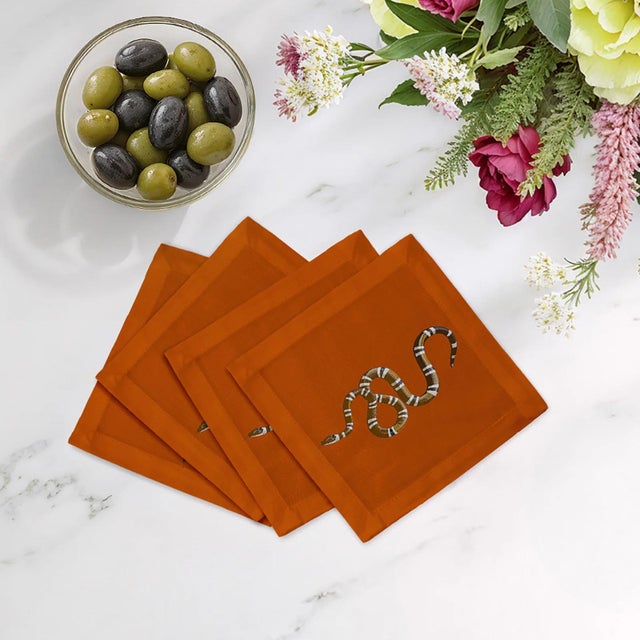 Serpent Cocktail Napkins feature entwined snake patterns that symbolize mystery, transformation, and strength. Designed in...